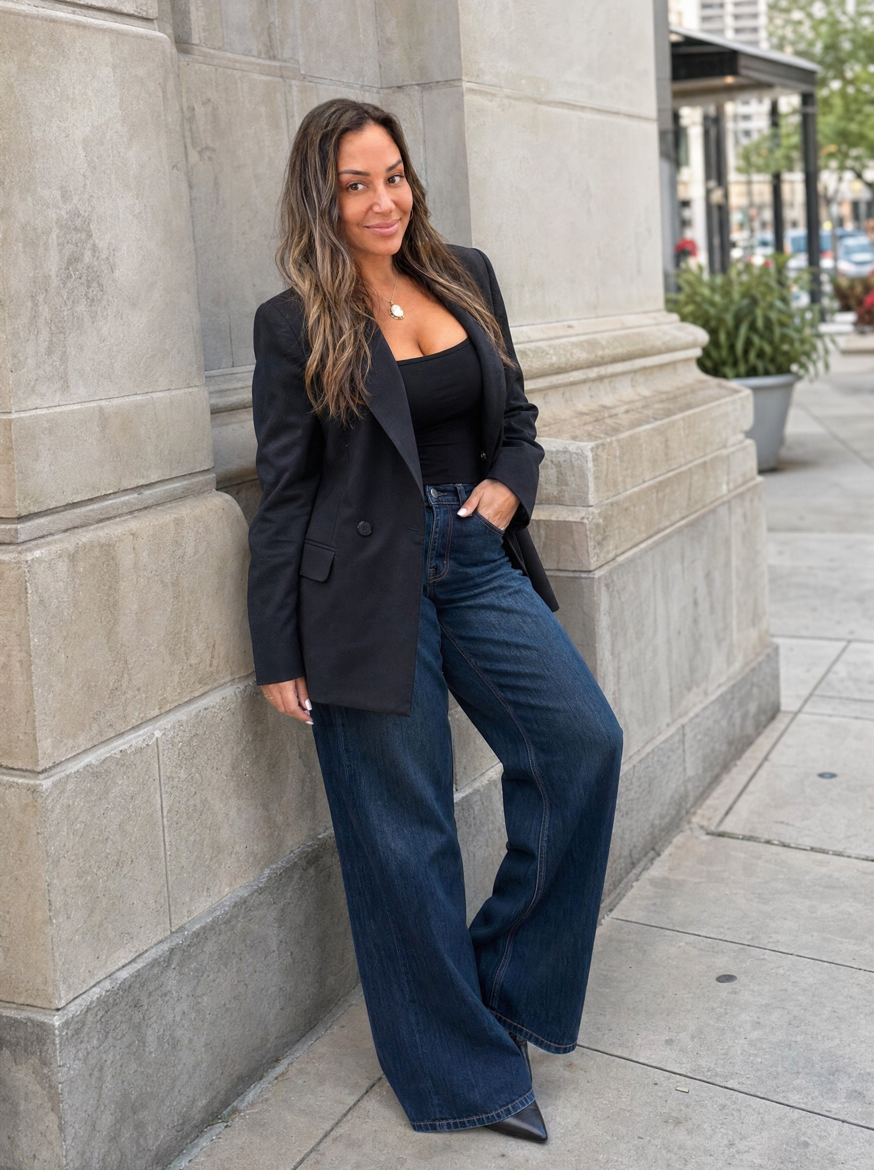 Martina Matthews in a black blazer and dark jeans, leaning against a stone building outdoors.